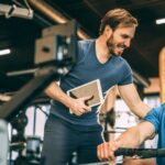 Partnership Marketing for Gyms – trainer guiding client during workout session in modern fitness center